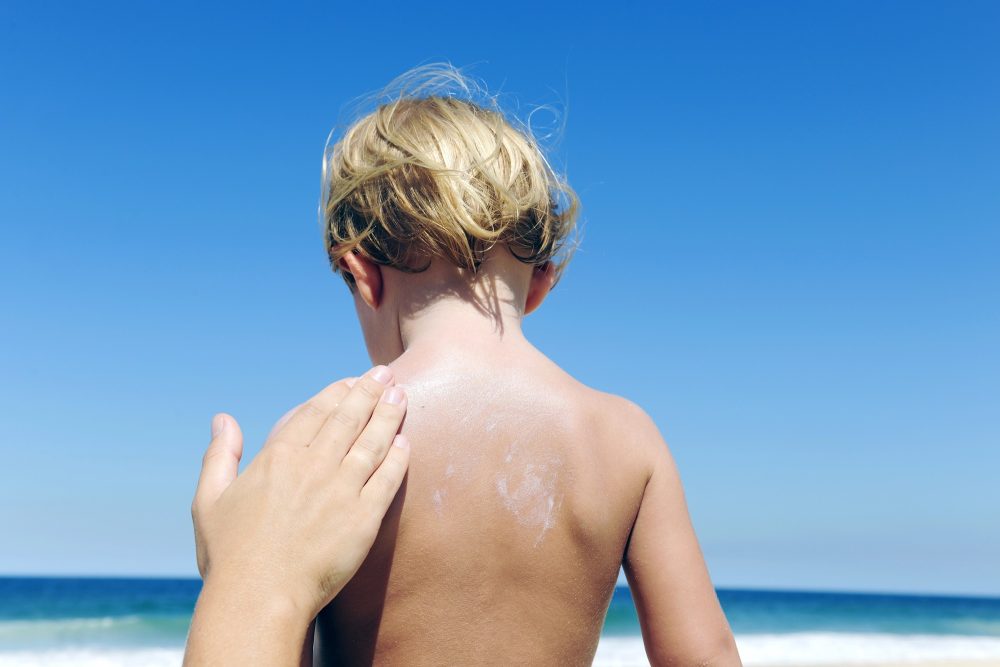 Mutter trägt Sonnencreme auf den Rücken der Kinder auf