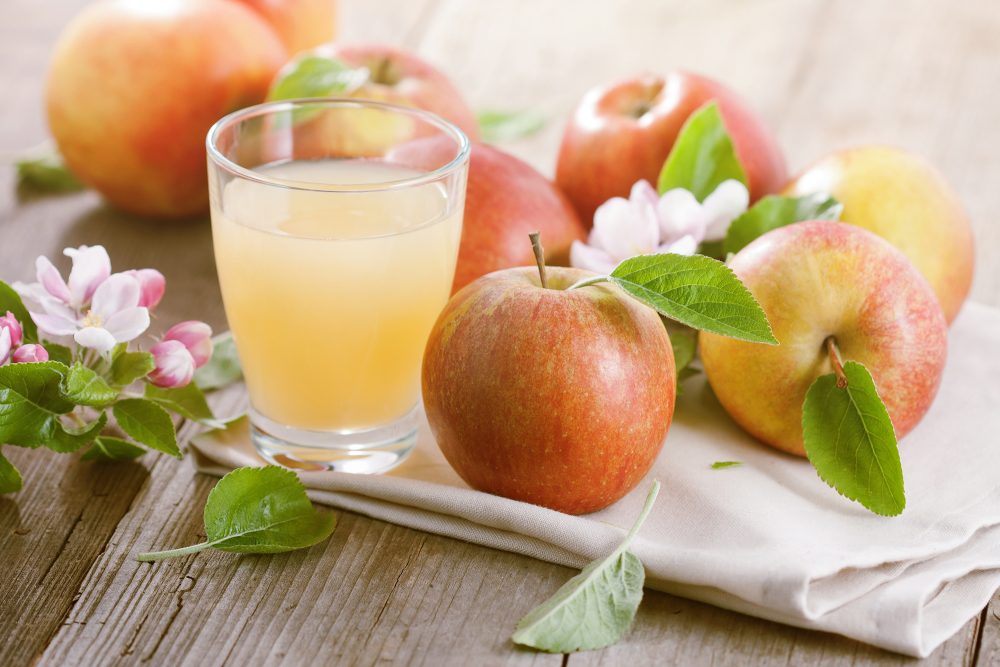 Glas frisch gepresster Apfelsaft mit Äpfeln und Apfelblüten