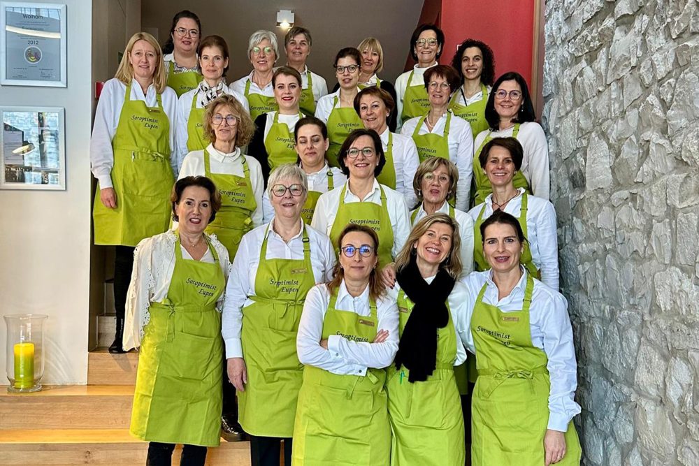 Gruppenbild von rund 20 Frauen, die eine neongrünfarbene Schürze mit der Aufschrift "Soroptimist Eupen" tragen und auf einer Treppe stehen