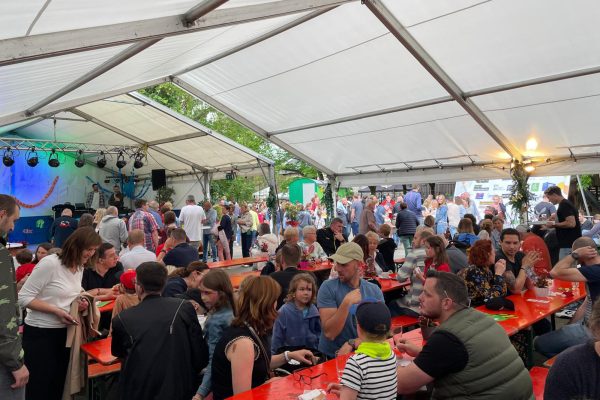 Schulfestbesucher sitzen im Festzelt an langen Tischen