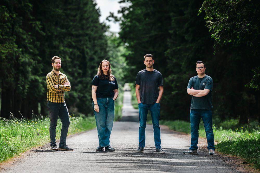 Die Band posiert für ein Gruppenfoto, die Bandmitglieder stehen auf einem Weg in einem Waldstück