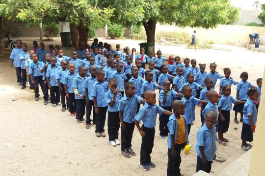 Kinder in Schuluniformen (blaues Hemd, schwarze Hose) stehen in Reih und Glied zusammen