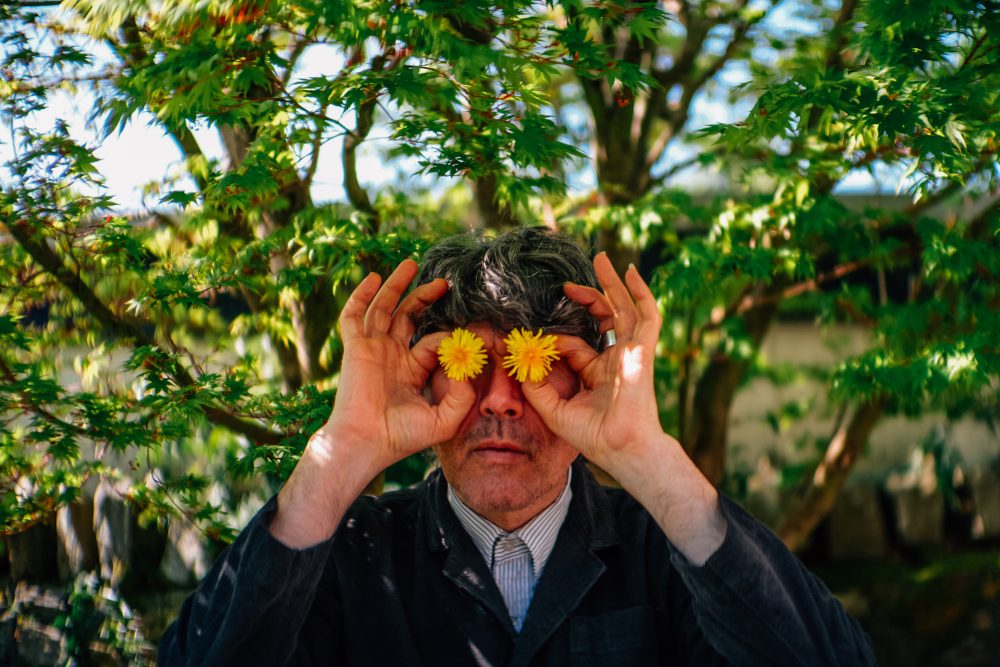 Porträt von Gruff Rhys, der sich zwei Löwenzahnblüten vor die Augen hält
