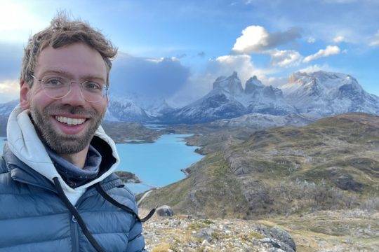 Stefan Pitz im Torres del Paine Nationalpark mit Panorama-Sicht auf einen Bergsee im Tal und hohe Berge im Hintergrund