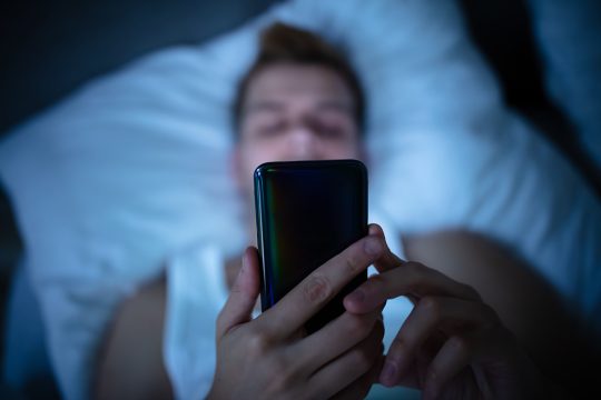 Jugendlicher oder Mann mit Smartphone in Bett