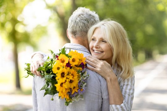 Frau mit Blumenstrauß in der Hand umarmt einen Mann